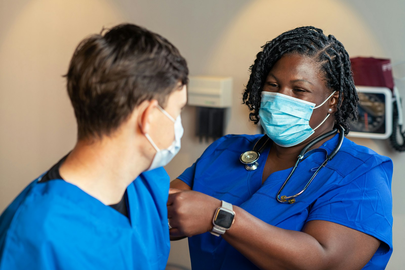 Two nurses in blue scrubs checking a smart watch together