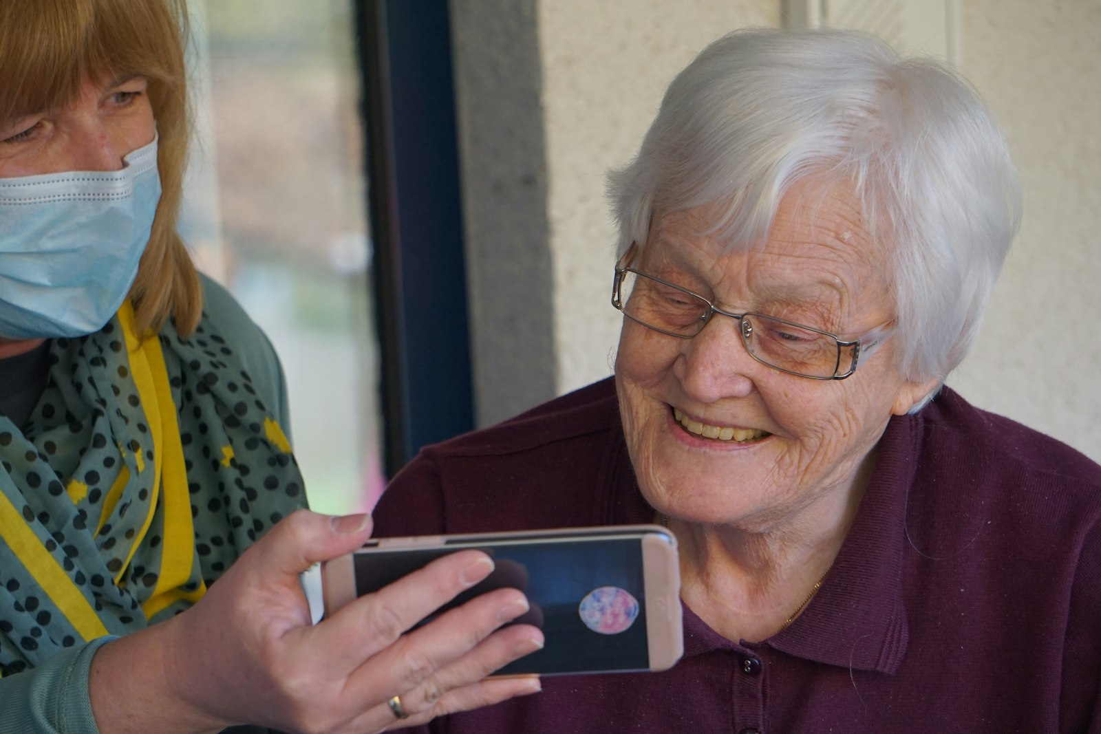 Older woman smiling at a phone with a nurse beside her